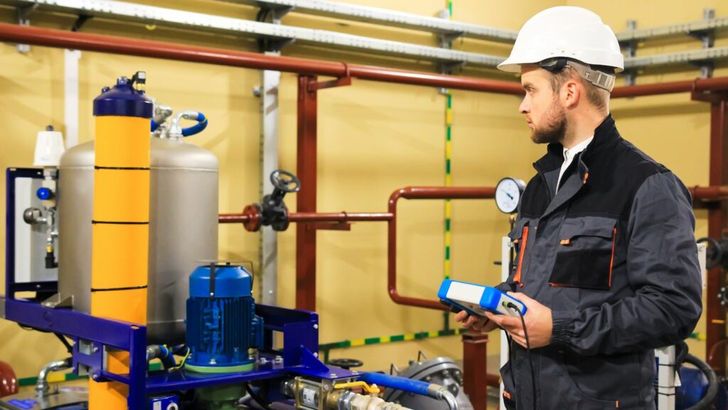 A professional plumber in a hard hat inspecting commercial plumbing systems with advanced tools, ensuring efficient preventative plumbing maintenance.